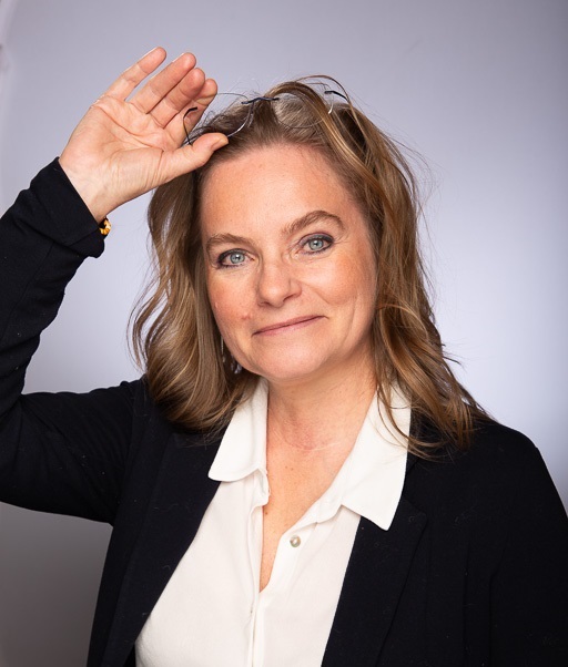 Portrait de Delphine Malapert, praticienne en PNL et formée en EMDR-DSA en Suisse romande, souriante, main levée vers la tête, sur fond neutre.